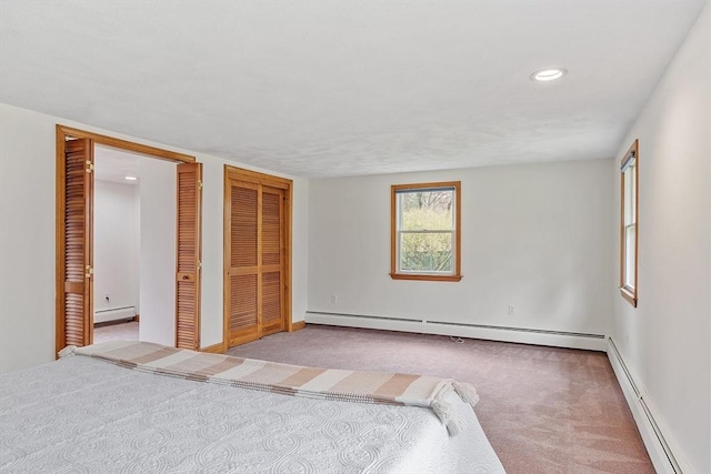 unfurnished bedroom with a baseboard radiator, carpet, and two closets