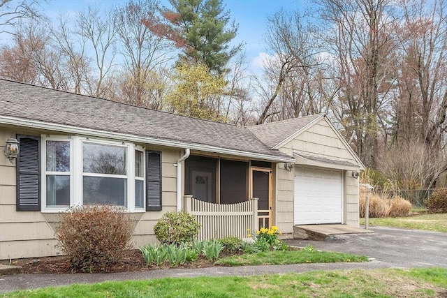 view of side of property with a garage, a shingled roof, and aphalt driveway