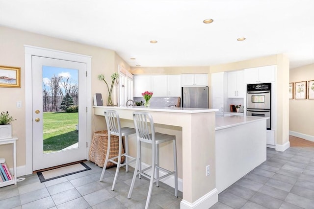 kitchen featuring a peninsula, a breakfast bar, light countertops, white cabinets, and stainless steel appliances