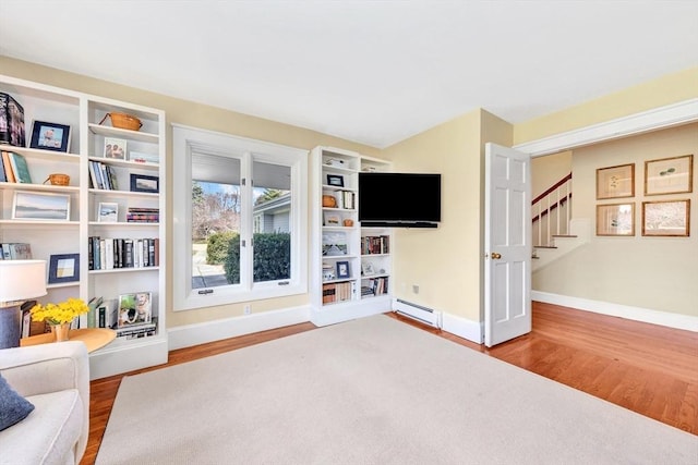 unfurnished living room featuring baseboards, a baseboard heating unit, wood finished floors, and stairway