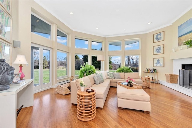 living area with recessed lighting, light wood-type flooring, a towering ceiling, a baseboard heating unit, and ornamental molding