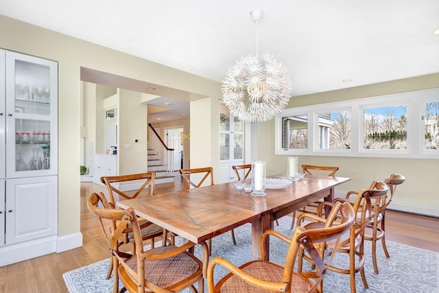 dining room featuring an inviting chandelier, light wood-style flooring, stairs, and baseboards