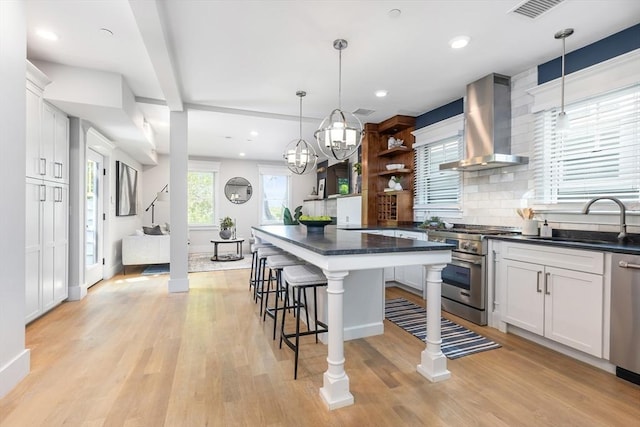 kitchen featuring wall chimney exhaust hood, appliances with stainless steel finishes, a sink, open shelves, and a kitchen bar
