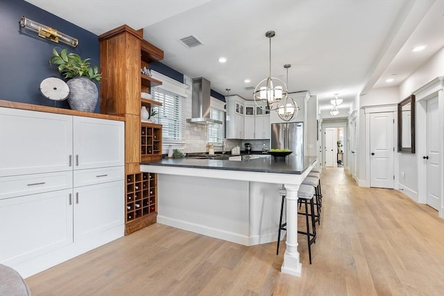 kitchen with wall chimney exhaust hood, freestanding refrigerator, open shelves, a peninsula, and light wood-type flooring