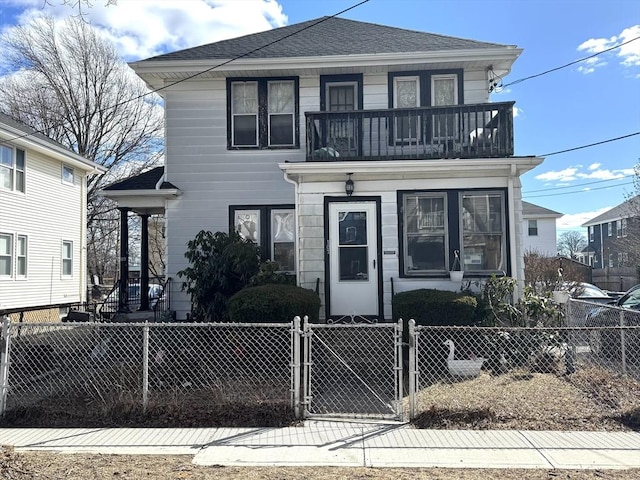 american foursquare style home with a fenced front yard, a gate, roof with shingles, and a balcony