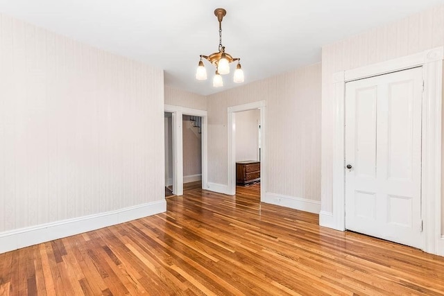 unfurnished dining area with light wood-type flooring, a chandelier, and baseboards