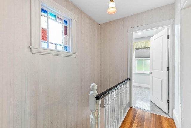 hallway with an upstairs landing, plenty of natural light, wood finished floors, and baseboards