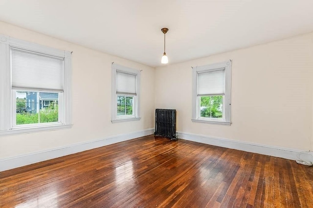 empty room featuring healthy amount of natural light, wood-type flooring, and radiator heating unit