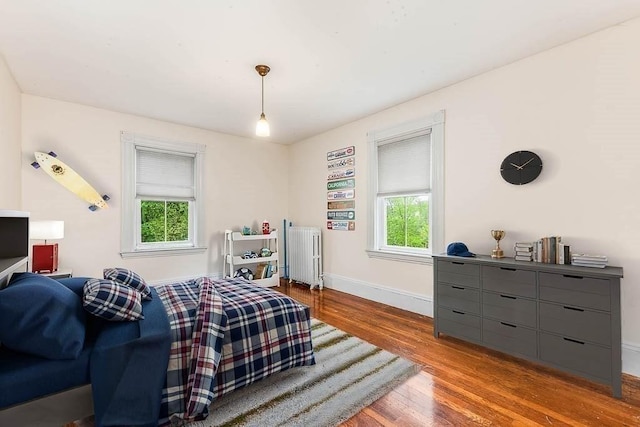 bedroom featuring radiator heating unit, wood finished floors, multiple windows, and baseboards