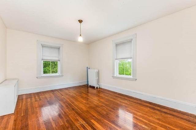 empty room featuring radiator, healthy amount of natural light, baseboards, and wood finished floors