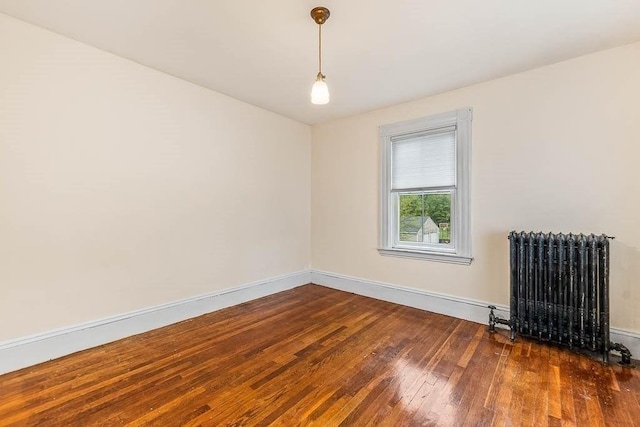 empty room with radiator, hardwood / wood-style flooring, and baseboards