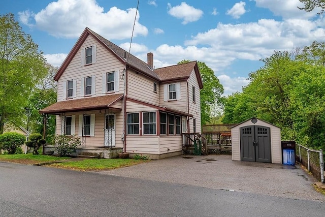 view of front of house with a storage unit, a chimney, an outdoor structure, a shingled roof, and covered porch