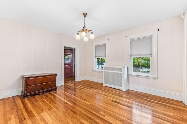 spare room featuring light wood finished floors, a chandelier, radiator heating unit, and baseboards