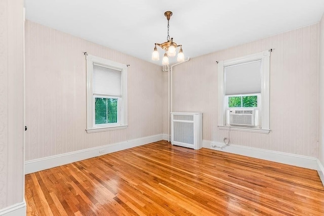 empty room with wood finished floors, a chandelier, baseboards, cooling unit, and heating unit