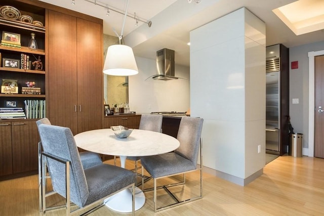 dining space featuring rail lighting, light wood-style flooring, and baseboards