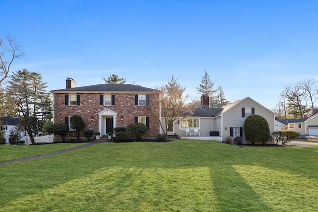 colonial house with a chimney, brick siding, and a front yard