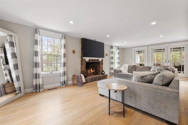 living room with baseboards, a stone fireplace, light wood-style flooring, and a healthy amount of sunlight
