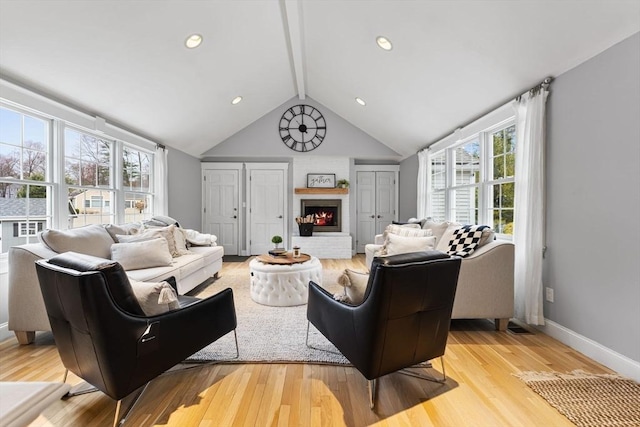 living room featuring plenty of natural light, vaulted ceiling with beams, a brick fireplace, and light wood-type flooring