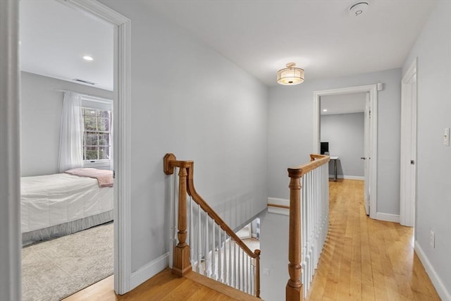 hallway featuring visible vents, light wood-style floors, baseboards, recessed lighting, and an upstairs landing