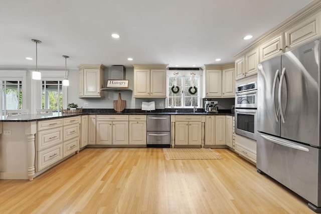 kitchen featuring stainless steel appliances, a sink, cream cabinetry, and wall chimney exhaust hood