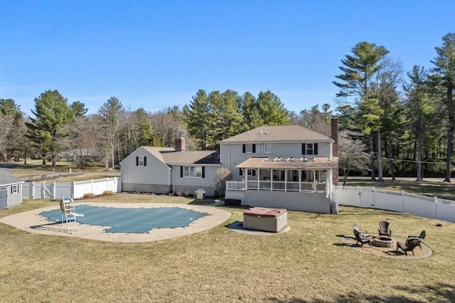 rear view of house with a fire pit, a fenced backyard, a chimney, a jacuzzi, and a yard
