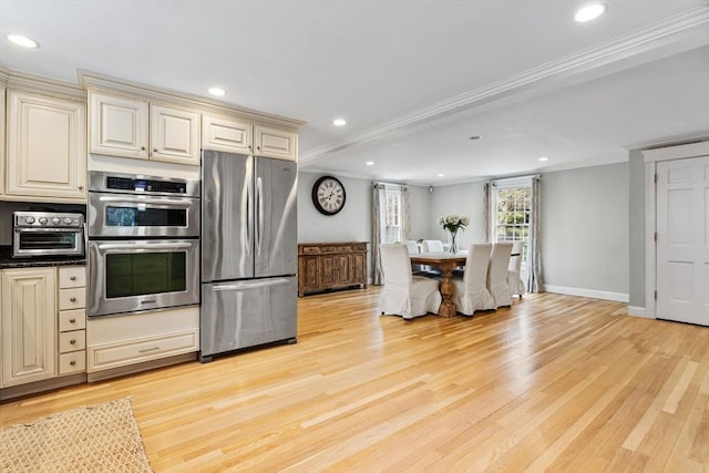 kitchen featuring a toaster, appliances with stainless steel finishes, cream cabinetry, and light wood-type flooring