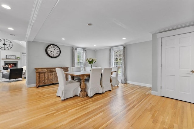 dining room featuring crown molding, baseboards, a warm lit fireplace, and light wood-style flooring
