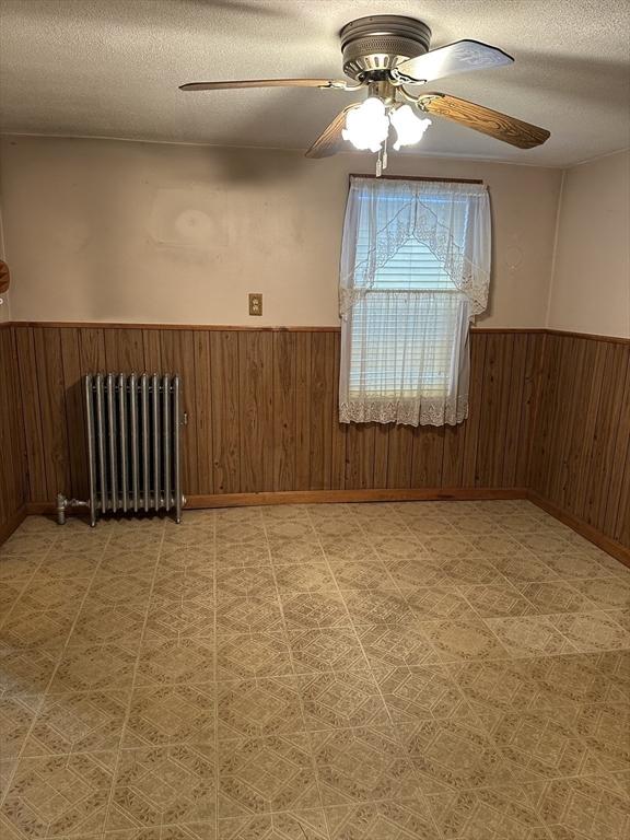50 Keene St, Lowell, MA 01852 - unfurnished room with radiator, wainscoting, a textured ceiling, wooden walls, and a ceiling fan
