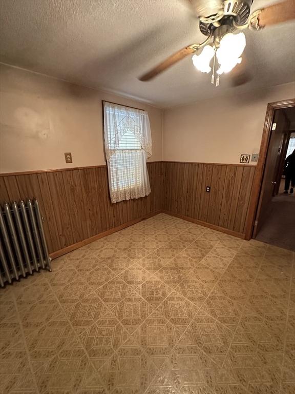50 Keene St, Lowell, MA 01852 - unfurnished room with a wainscoted wall, wooden walls, a textured ceiling, a ceiling fan, and radiator