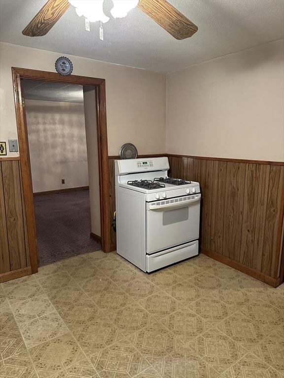 50 Keene St, Lowell, MA 01852 - kitchen featuring white gas stove, a ceiling fan, wainscoting, light floors, and wood walls