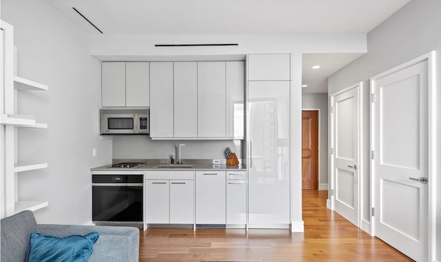 kitchen with appliances with stainless steel finishes, light wood-type flooring, white cabinetry, and sink