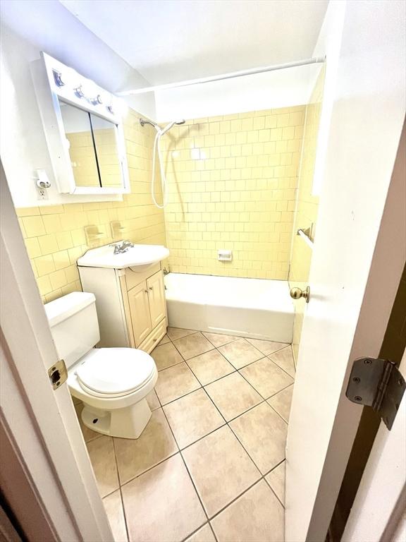 full bathroom featuring vanity, tile patterned flooring, tiled shower / bath combo, toilet, and tile walls