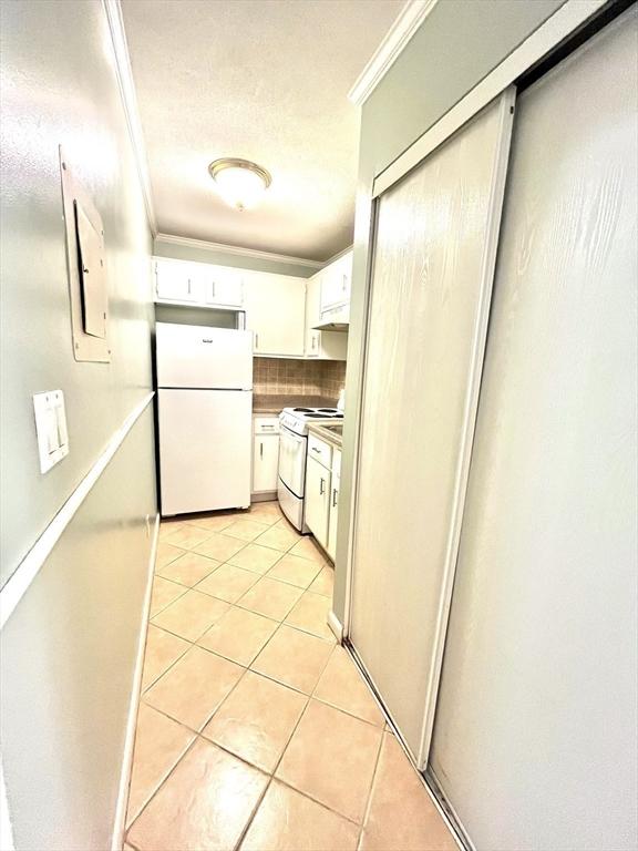 kitchen featuring white appliances, backsplash, white cabinets, crown molding, and light tile patterned floors