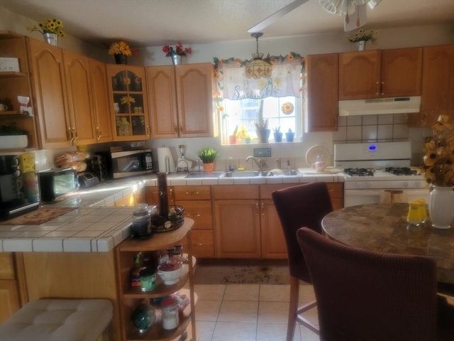 kitchen with light tile patterned flooring, sink, tile countertops, and white gas range