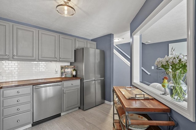 kitchen featuring gray cabinets, stainless steel appliances, tasteful backsplash, light hardwood / wood-style floors, and wood counters