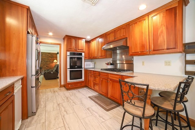 40 Old Stage Rd, Chelmsford, MA 01824 - kitchen featuring under cabinet range hood, appliances with stainless steel finishes, brown cabinets, a peninsula, and recessed lighting