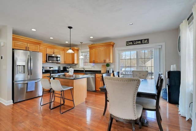 kitchen with stainless steel appliances, dark countertops, hanging light fixtures, a kitchen island, and light wood-type flooring