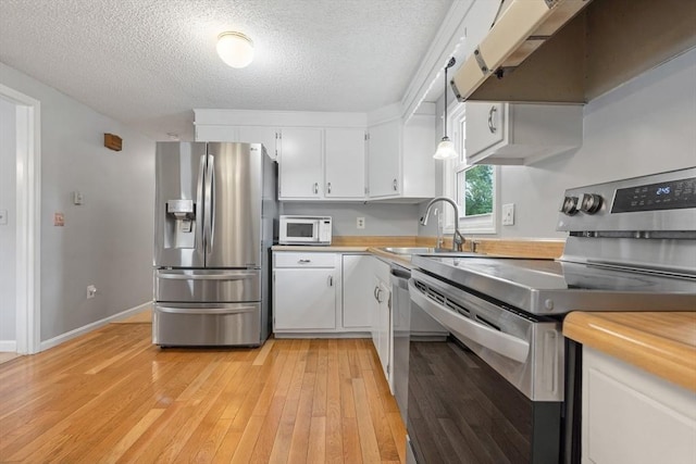 kitchen featuring white cabinets, light wood-style floors, appliances with stainless steel finishes, under cabinet range hood, and a sink