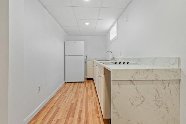 kitchen featuring a paneled ceiling, light countertops, light wood-style floors, freestanding refrigerator, and baseboards