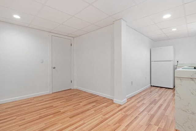 spare room with light wood finished floors, baseboards, and a drop ceiling