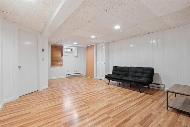 living area with a baseboard heating unit, a drop ceiling, and wood finished floors