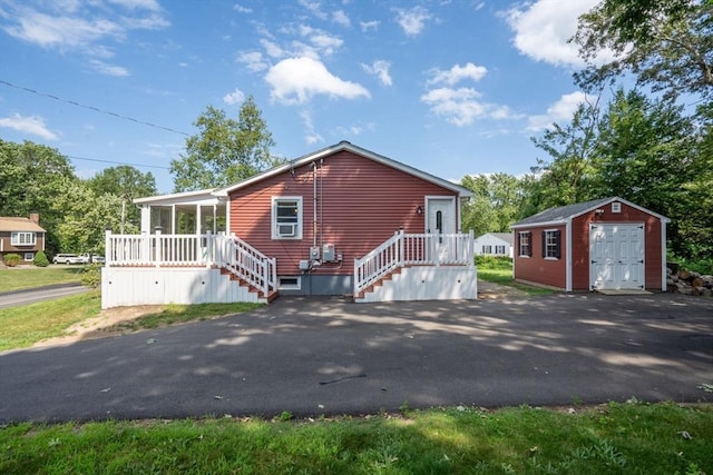 view of front facade with aphalt driveway, an outbuilding, a sunroom, and a storage unit