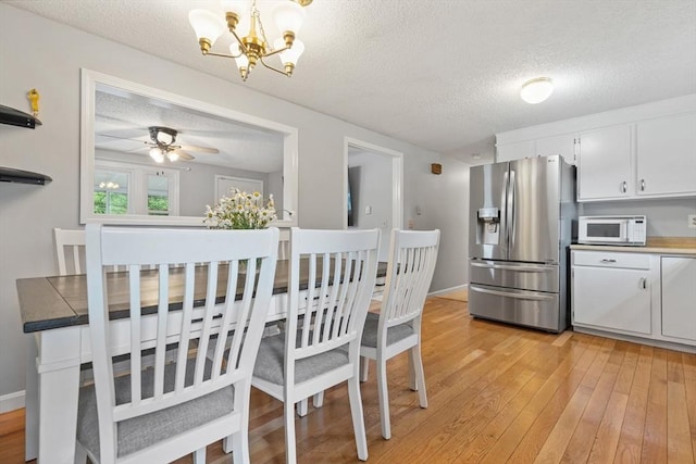 dining area featuring a textured ceiling, ceiling fan with notable chandelier, light wood-type flooring, and baseboards