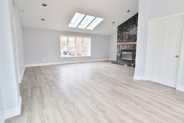 unfurnished living room featuring a skylight, a high end fireplace, light wood-style flooring, vaulted ceiling, and baseboards