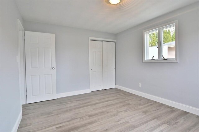 unfurnished bedroom featuring baseboards, light wood-style flooring, and a closet