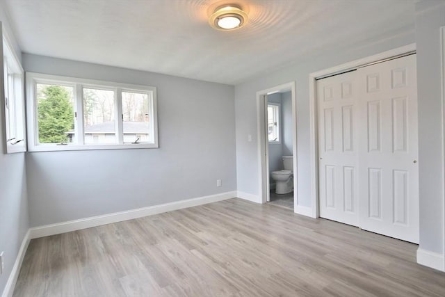 unfurnished bedroom with light wood-type flooring, a closet, baseboards, and ensuite bath
