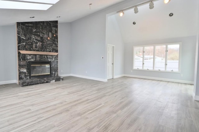 unfurnished living room with wood finished floors, a premium fireplace, baseboards, a skylight, and high vaulted ceiling
