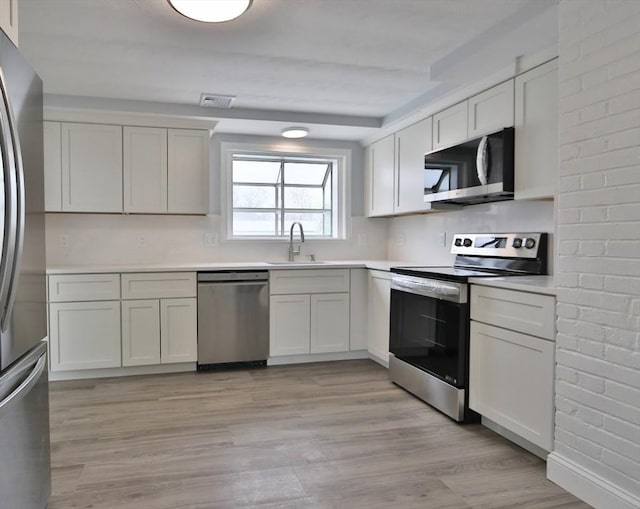 kitchen featuring appliances with stainless steel finishes, a sink, light wood-style flooring, and light countertops