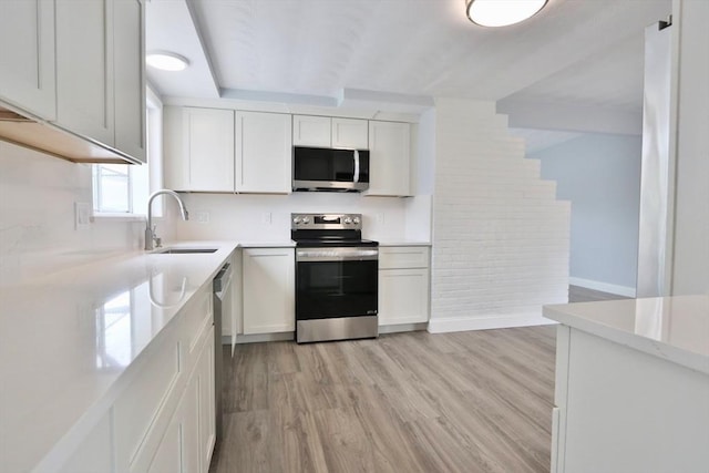 kitchen with appliances with stainless steel finishes, a sink, light wood-style flooring, light countertops, and white cabinets