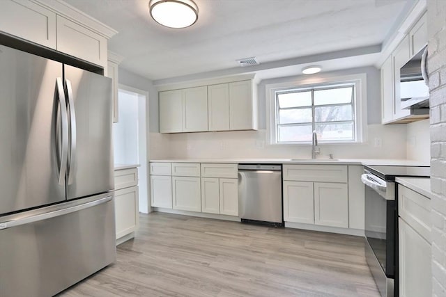 kitchen featuring stainless steel appliances, a sink, light countertops, and light wood finished floors